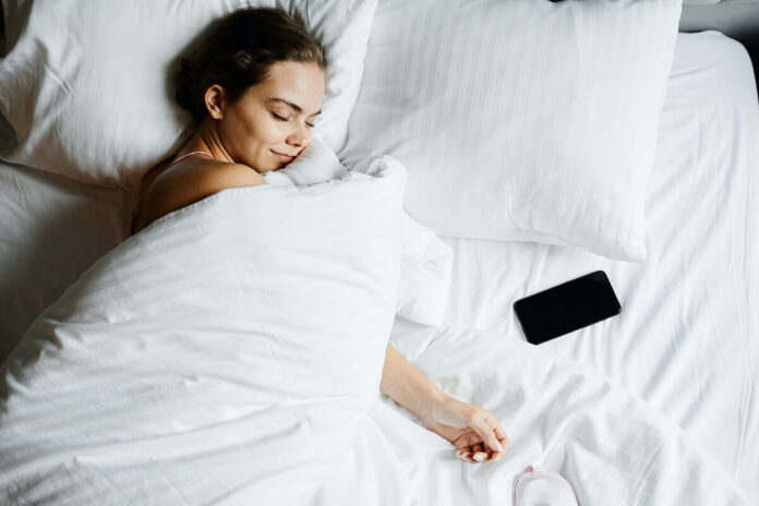 A woman sleeping on her mattress beside her mobile phone