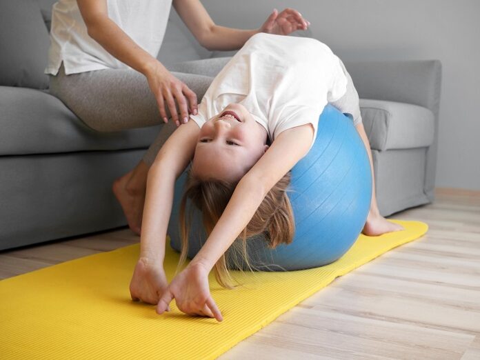 mother helping girl exercise ball